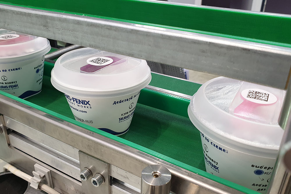 Верхнее нанесение  стикеров с кодом дата матрикс на цилиндрические упаковки йогуртов