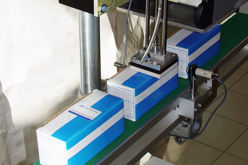 Образец нанесения этикеток сверху на синии коробки пневморукой принтера Novexx